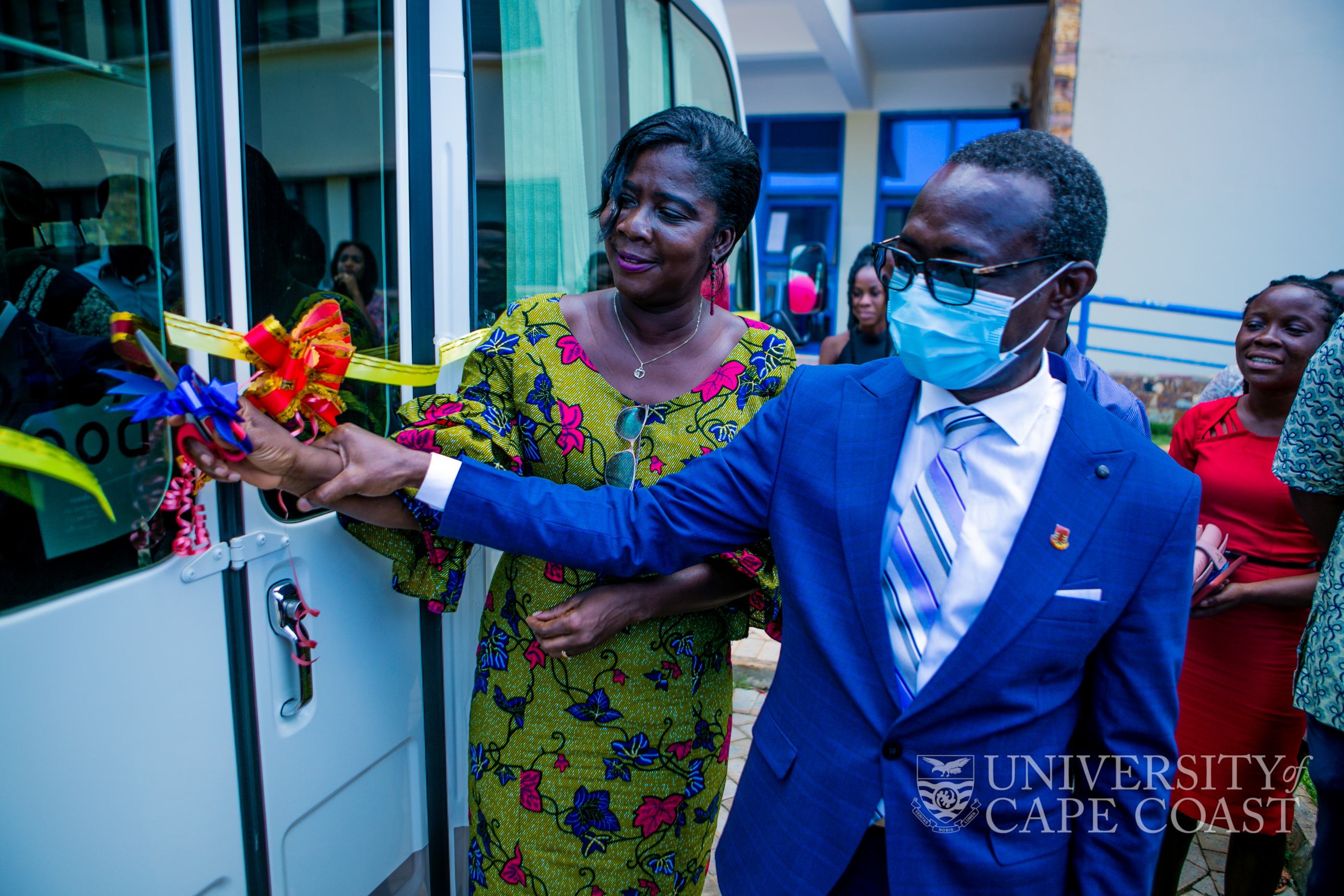 Pro Vice-Chancellor of UCC, Prof. Rosemond Boohene, being assisted by the Vice-Chancellor to cut the tape to commission the bus